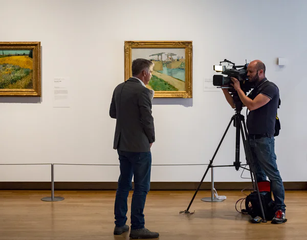 Een tv-presentator wordt gefilmd voor twee schilderijen van Vincent van Gogh: De brug van Langlois en Korenveld. Foto: Jan-Kees Steenman